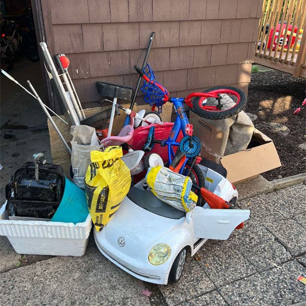 Abandoned toys and junk piled outside a wooden shed, including a toy car and bicycles.